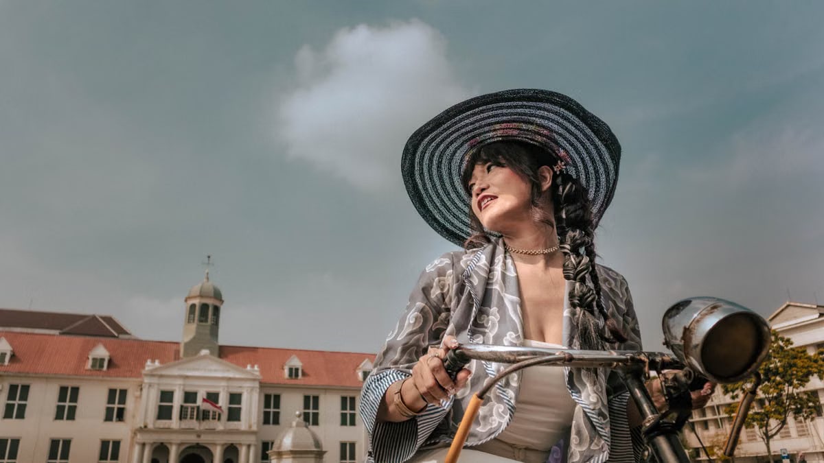 A fashionable woman on a vintage bike, with Jakarta's Fatahillah Square as the backdrop.