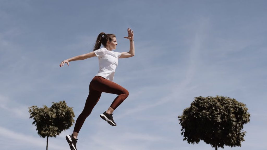 Athletic woman in action jump against a blue sky background. Captures fitness in motion.